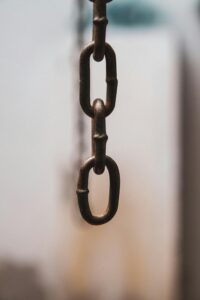 Detailed view of an iron chain link hanging vertically with a soft focus background.