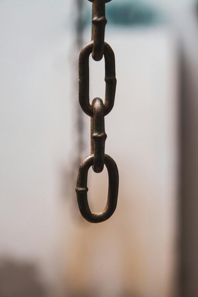 Detailed view of an iron chain link hanging vertically with a soft focus background. links