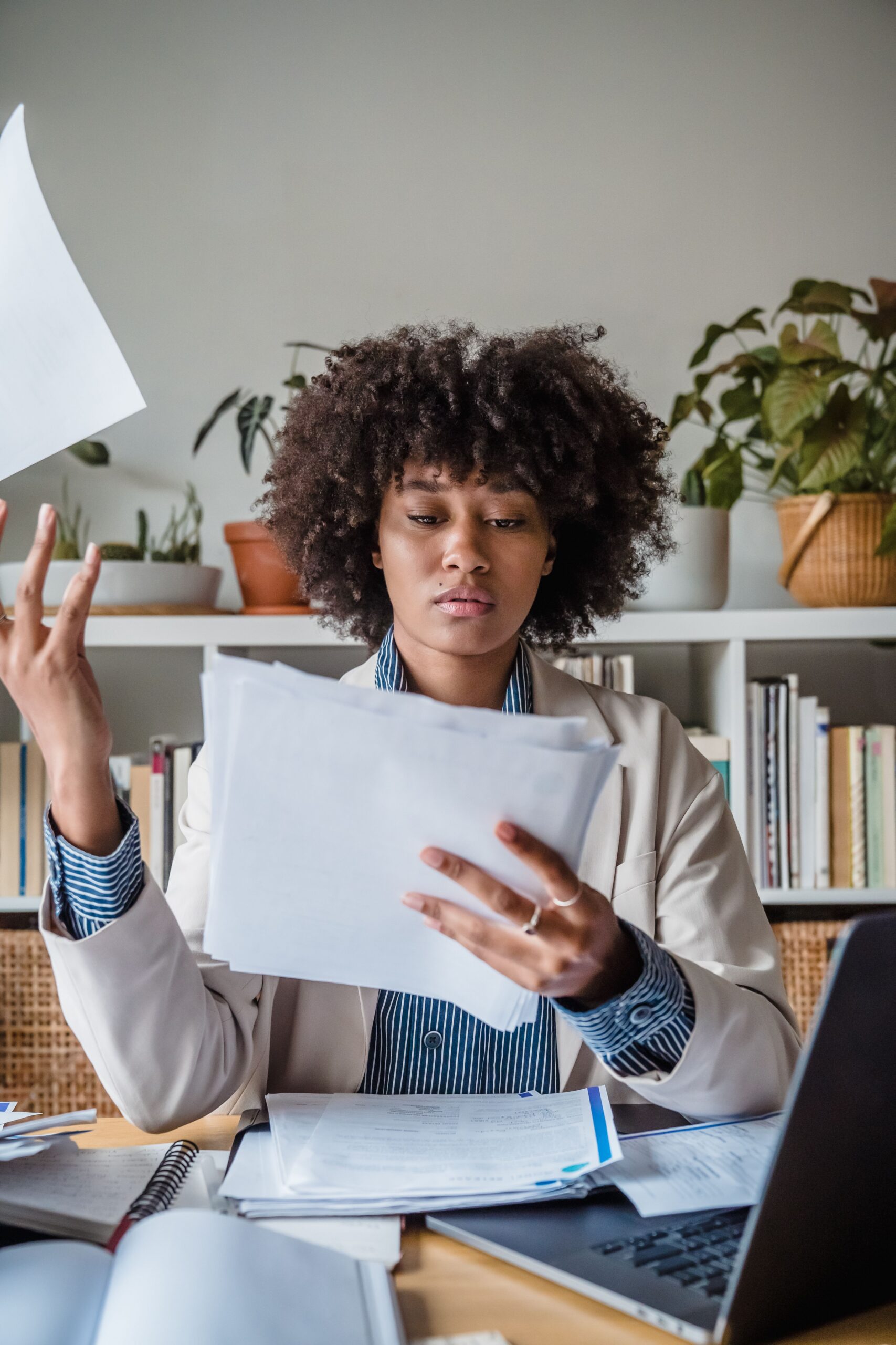 Young woman managing documents in a home office, surrounded by plants and laptop.