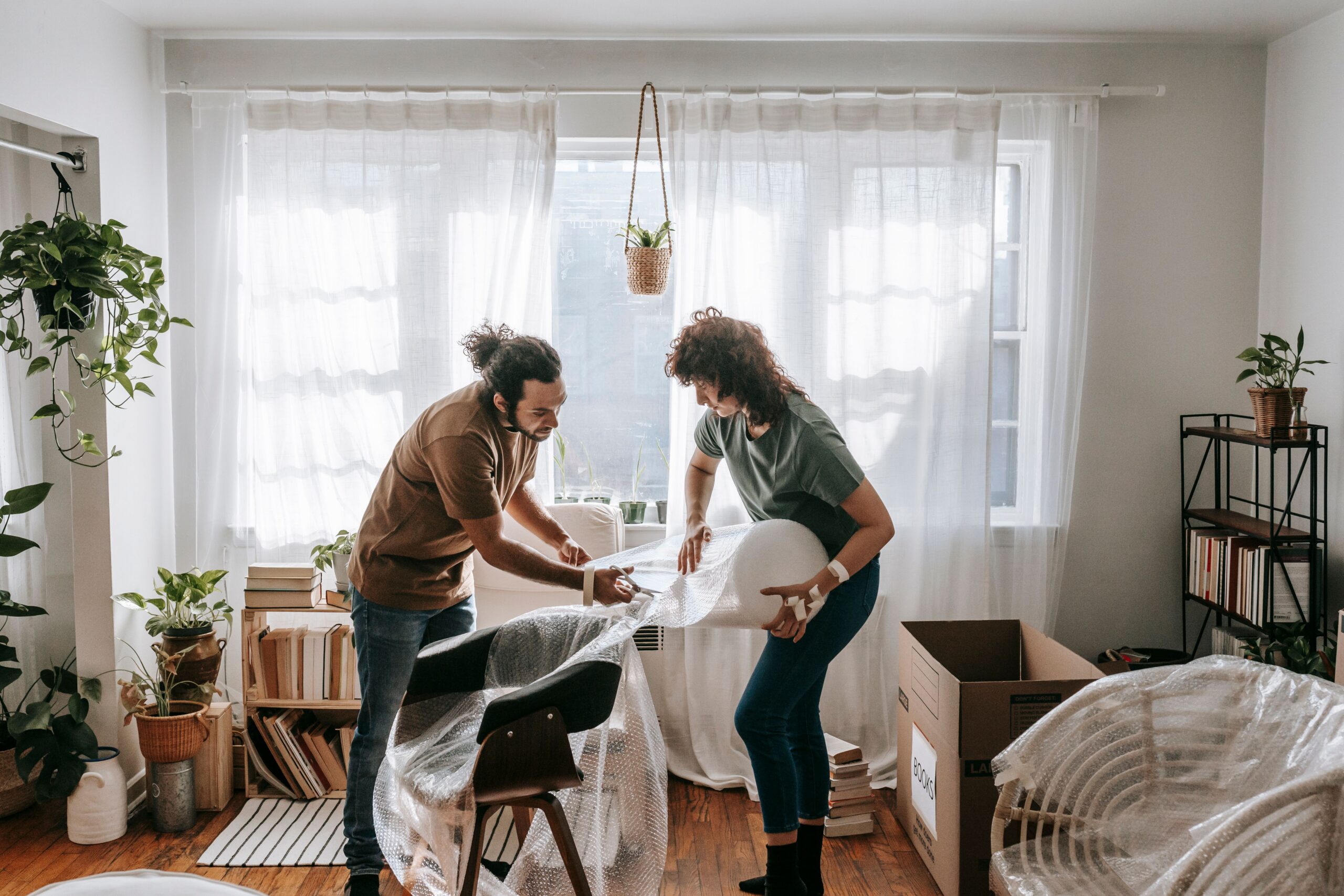 A couple joyfully packing furniture with bubble wrap in a bright, modern living room.